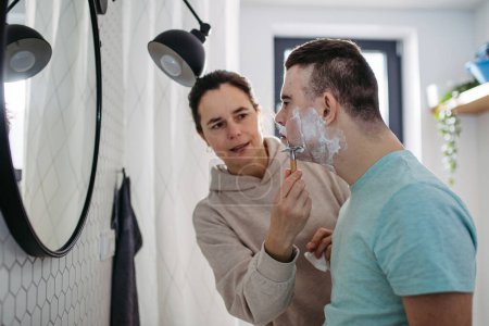 Photo for Mother applying shaving foam on sons face. Young man with down syndrome learning how to shave. Concept of mothers day and motherly love. - Royalty Free Image