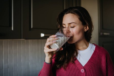 Beautiful woman drinking a glass of plant-based milk in the kitchen.