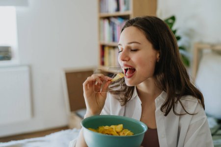 Enjoying crunchy chips. Woman has cravings for potato chips, eating with closed eyes, holding bowl full of crisps.