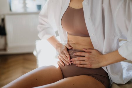 Woman at home suffering from menstrual pain, having period cramps. Close up of woman holding abdomen, endometriosis, and conditions causing pain in tummy.