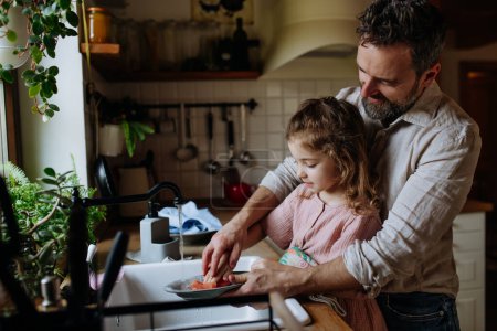 Vater und Tochter kochen gemeinsam in der Küche, putzen Obst in der Spüle. Mädchen Papa. Bedingungslose Vaterliebe und Vatertagskonzept.