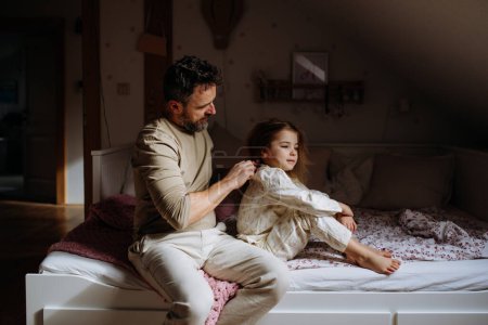Père tressant les cheveux de ses filles, peignant les cheveux dans le cadre de la routine du coucher. Papa célibataire prenant soin de sa coiffure de filles.