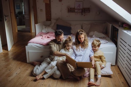 Hermosa familia sentada en la habitación de los niños en el suelo, mirando viejas fotos familiares en el fotoálbum. Calma hygge momento familiar.