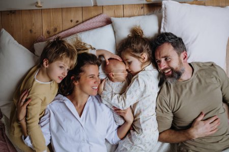 Draufsicht auf eine Familie, die mit Kindern und Neugeborenem im Bett liegt. Perfekter Moment. Starke Familie, Bindung, bedingungslose Liebe der Eltern zu ihren Kindern.