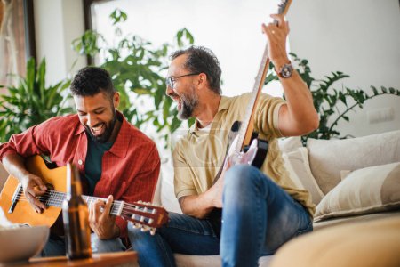 Best friends, musician jamming together. Playing music on acoustic and electric guitar together, having beer and fun. Concept of male friendship, bromance.