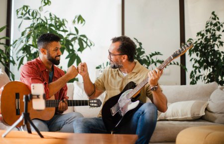Beste Freunde, Musiker jammen zusammen, drehen Videos in den sozialen Medien. Gemeinsam Musik auf akustischer und elektrischer Gitarre zu Hause für Fans zu spielen. Konzept der Männerfreundschaft, Bromance.