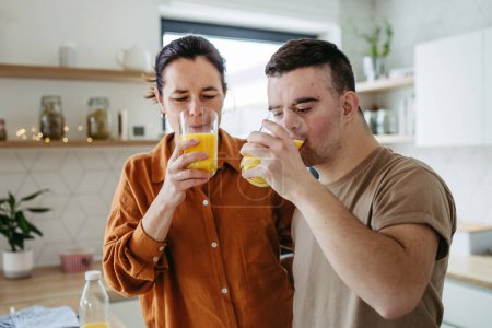 Portrait d'un jeune homme trisomique avec sa mère à la maison, trinquant et buvant du jus d'orange. routine du matin pour les hommes atteints de syndrome de Down trouble génétique.