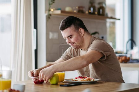 Photo for Young man with Down syndrome preparing breakfast on his own. Morning routine for man with Down syndrome genetic disorder. - Royalty Free Image