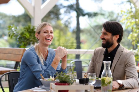 Téléchargez les photos : Couple assis à l'extérieur sur la terrasse restaurant, ayant rendez-vous romantique dîner, rire. Déjeuner d'affaires pour deux gestionnaires, discussion sur un nouveau projet d'entreprise. - en image libre de droit