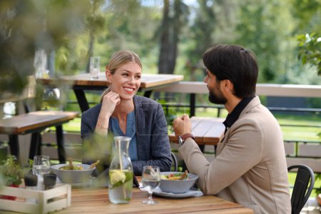 Photo for Couple sitting outdoors on terrace restaurant, having romantic dinner date. Business lunch for two managers, discussing new business project. - Royalty Free Image