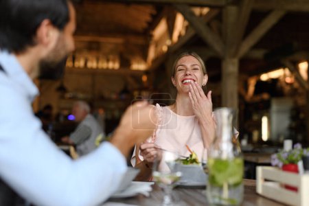 Photo for Happy loving couple at date in restaurant. Husband and wife sitting at table, laughing, having brunch, lunch in modern cafe. - Royalty Free Image