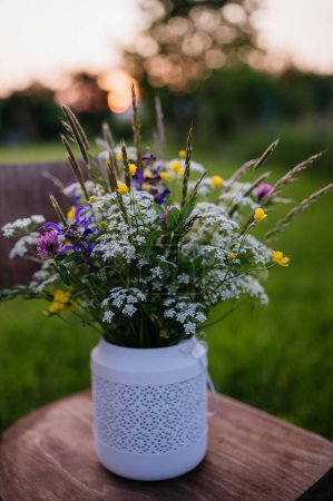 Weiße Vase voller Wiesenblumen, Kräuter und Gras, im Freien. Eine bunte Vielfalt sommerlicher Wildblumen.