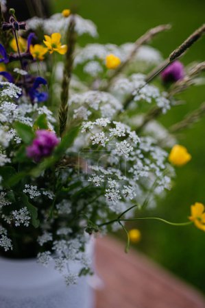 Téléchargez les photos : Vase blanc plein de fleurs de prairie, herbes et herbe, en plein air. Une variété colorée de fleurs sauvages d'été. - en image libre de droit