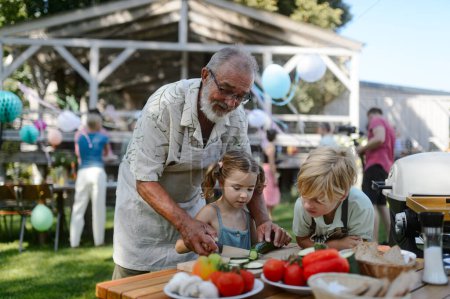 Photo for Grandfather teaching kids to cut vegetables for grilling. Grilling together at garden BBQ. Grandchildren with grandfatehr at summer family garden party. - Royalty Free Image