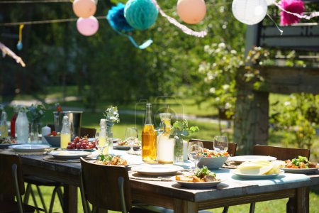 Gros plan d'une table dressée lors d'une garden party d'été, de la nourriture grillée. Cadre de table avec verres, limonade, décoration florale et papier délicate, et bouteilles de vin d'été.