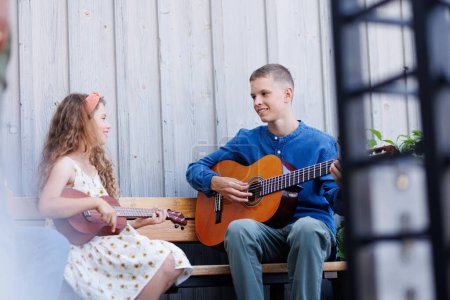 Foto de Chico y chica tocando guitarras acusticas, haciendo música juntos. Hermosa música de jóvenes adolescentes. Sentado al aire libre. - Imagen libre de derechos