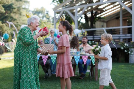 Photo for Garden birthday party for senior lady. Beautiful senior birthday woman receiving gift and flowers from grandchildren. - Royalty Free Image