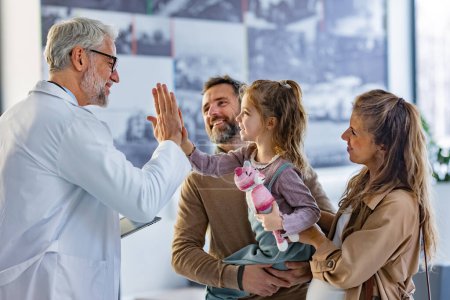 Photo for Friendly pediatrician giving high five to little patient. Parents with girl patient greeting doctor in hospital corridor. Concept of children healthcare and emotional support for child patients. - Royalty Free Image