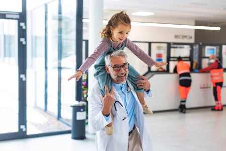 Porträt eines Kinderarztes mit einem kleinen Patienten, der huckepack auf seinen Schultern sitzt. Arzt trägt Mädchen auf Schultern. Freundschaftliche Beziehung zwischen Arzt und Patient.