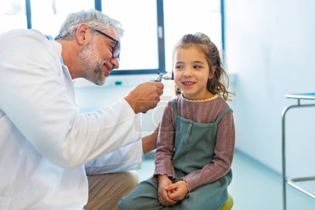 Primer plano del médico examinando las niñas oreja utilizando otoscopio, en busca de infección del oído. Relación amistosa entre el médico y el paciente infantil.