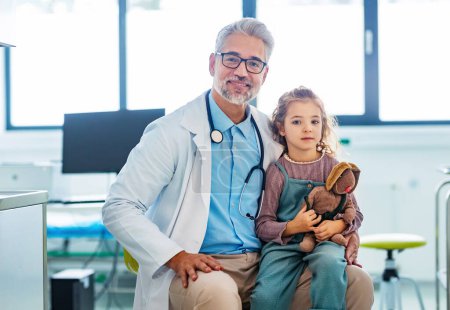 Porträt eines Kinderarztes mit einer kleinen Patientin auf dem Knie. Freundschaftliche Beziehung zwischen Arzt und Patient.