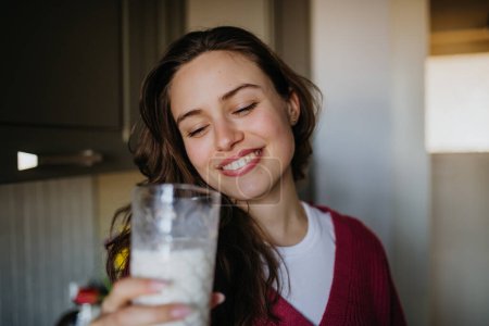 Beautiful woman drinking a glass of plant-based milk in the kitchen.