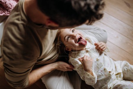 Top view of father with daughter on floor laughing together, having fun and making faces. Girls dad. Unconditional paternal love, Fathers Day concept.