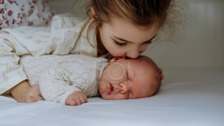 Photo for Portrait of big sister cuddling newborn, little baby. Girl kissing her sleeping new sibling in bed. Sisterly love, joy for the new family member. - Royalty Free Image