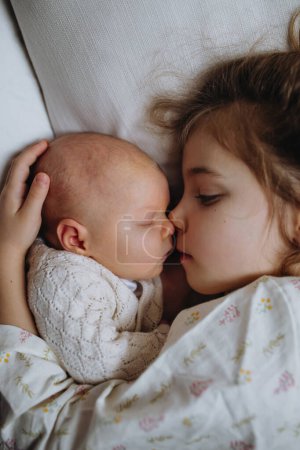 Porträt der großen Schwester beim Kuscheln mit Neugeborenem, kleinem Baby. Mädchen liegt mit ihrem neuen Geschwisterchen im Bett, die Augen geschlossen. Schwesternliebe, Freude für das neue Familienmitglied.