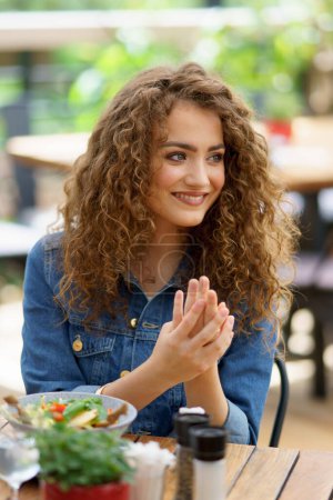 Photo for Beautiful woman sanitizing her hands with disinfectant gel in a restaurant before eating. Having lunch or brunch outdoors in restaurant patio. - Royalty Free Image