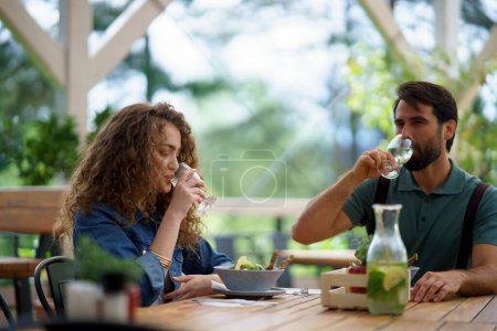 Foto de Pareja joven en la fecha en el restaurante, sentado en la terraza del restaurante, agua potable. Novio y novia disfrutando la primavera, almorzando o almorzando al aire libre, asientos al aire libre para cenar. - Imagen libre de derechos