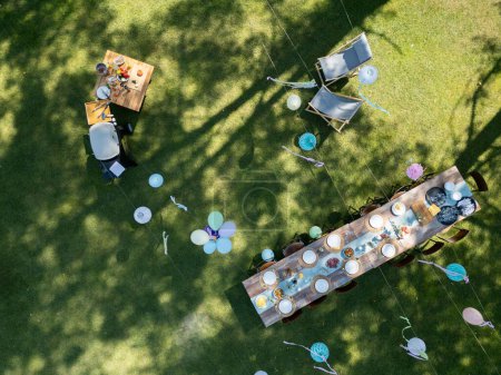Top view of summer garden party in a beautiful garden. BBQ family gathering, with a set table and colorful decorations.