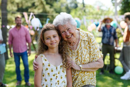 Photo for Portrait of young girl with grandmother at garden party. Love and closeness between grandparent and grandchild. - Royalty Free Image