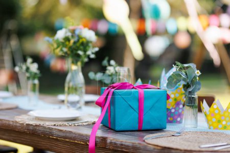 Close up of a birthday gift in blue wrapping paper with pink ribbon. Summer garden birthday party in a beautiful garden.