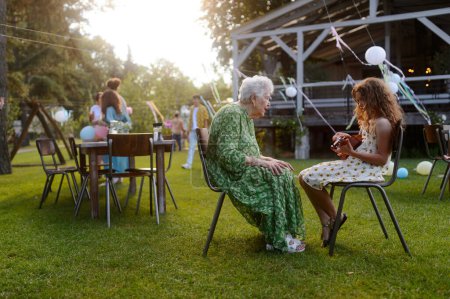 Photo for Girl playing on guitar for grandmother at garden party. Love and closeness between grandparent and grandchild. - Royalty Free Image