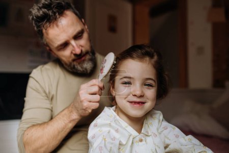 Father braiding his daughters hair, combing hair as part of bedtime routine. Single dad taking care of his daughters hairstyle.