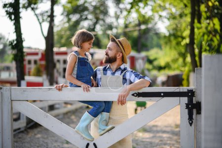 Foto de Retrato de familia campesina, padre con hija sentada en una cerca de madera en una granja familiar. Concepto de agricultura multigeneracional. - Imagen libre de derechos