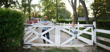 Téléchargez les photos : Portrait d'une famille d'agriculteurs, père et jeune fille debout sur une clôture en bois dans une ferme familiale. Concept d'agriculture multigénérationnelle. - en image libre de droit