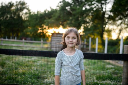 Téléchargez les photos : Belle jeune fille debout sur la prairie pendant le coucher du soleil, aidant sur la ferme familiale pendant l'été. - en image libre de droit