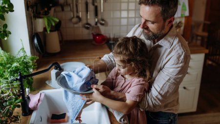 Vater und Tochter trocknen Geschirr mit Handtüchern, nachdem sie es gemeinsam gewaschen haben. Mädchen Papa. Bedingungslose Vaterliebe und Vatertagskonzept.