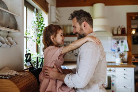 Tochter umarmt Vater liebevoll, sitzt auf Küchentisch. Bedingungslose Vaterliebe und Vatertagskonzept.