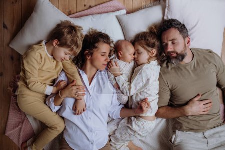 Draufsicht auf die Familie, die mit Kindern und Neugeborenem im Bett schläft. Perfekter Moment. Starke Familie, Bindung, bedingungslose Liebe der Eltern zu ihren Kindern.