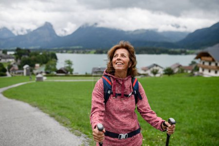 Téléchargez les photos : Portrait de belle femme âgée marchant à l'extérieur avec des bâtons de trekking, allant sur le sentier de randonnée. Touristes seniors profitant de la vue. - en image libre de droit