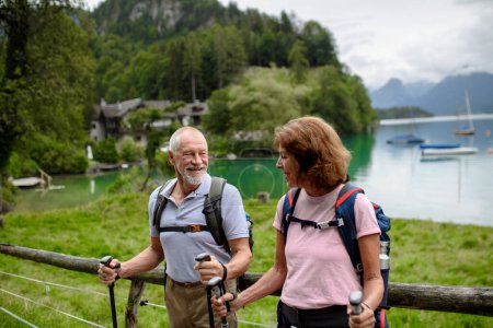 Foto de Retrato de pareja de ancianos activos caminando juntos en las montañas de otoño. Turistas mayores mirando el lago. - Imagen libre de derechos
