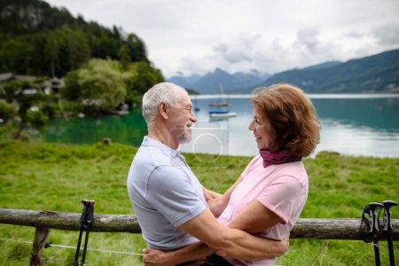 Foto de Retrato de pareja de ancianos enamorados haciendo senderismo juntos en las montañas. Turistas mayores abrazándose, yendo a besarse. Vista lateral. - Imagen libre de derechos