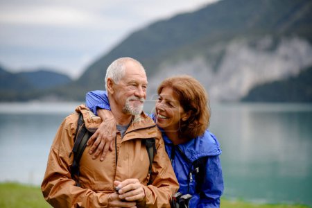Téléchargez les photos : Portrait d'un beau couple de personnes âgées actives marchant ensemble dans les montagnes d'automne. Touristes seniors s'embrassant devant un lac. - en image libre de droit