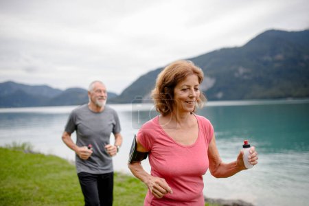 Foto de Pareja mayor corriendo por el lago en la naturaleza. Ancianos marido y mujer pasar unas vacaciones activas en las montañas, disfrutar de la actividad física y la relajación al aire libre. - Imagen libre de derechos