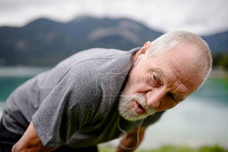 Téléchargez les photos : Respiration senior après course au bord du lac dans la nature. Homme âgé faisant de l'exercice pour rester en bonne santé, vital, faisant de l'activité physique, se relaxant à l'extérieur. - en image libre de droit