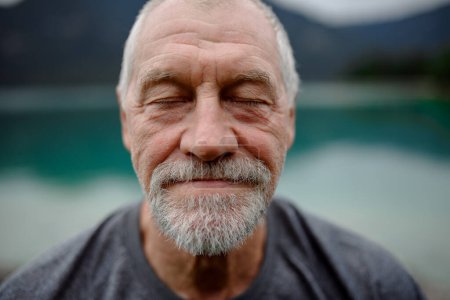 Porträt eines aktiven Seniors, der sich nach einer Bergwanderung ausruht. Nachdenklicher älterer Mann genießt friedliche, unberührte Natur.