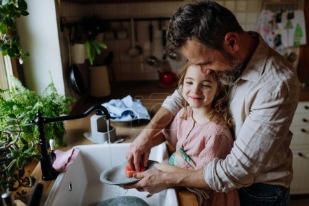 Papá y su linda hija lavando platos en el fregadero juntos. Chicas papá. Amor paterno incondicional, concepto del Día del Padre.
